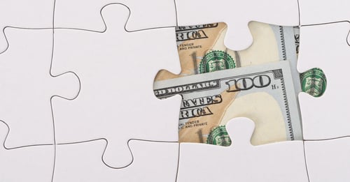 Puzzle with piece missing revealing hundred dollar bills underneath
