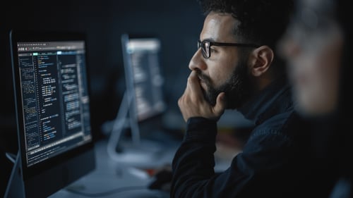 Male with beard and glasses studying computer screen in dark room