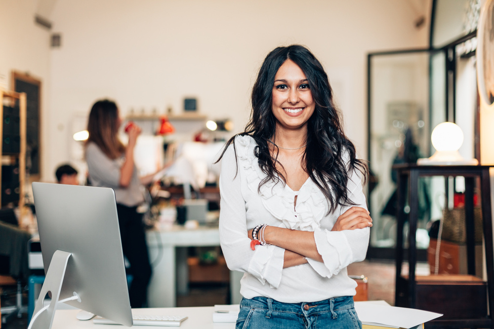 Smiling female small business profession next to desk with computer