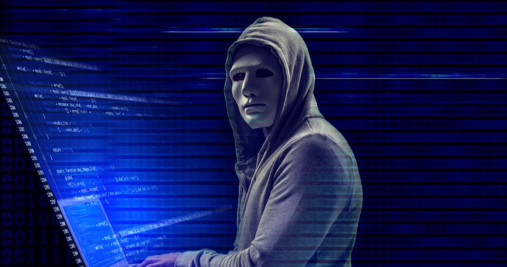 Hooded hacker wearing a mask working on laptop